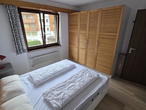 A bedroom with a bed, a window, a radiator, and a wooden wardrobe. - Floralp 5 # 4-bed apartment, Bad, WC 4-Bettwohnung, Bad, WC by Interhome (Leukerbad)