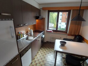 Une cuisine de taille réduite, équipée d’une cuisinière, d’un évier et d’une fenêtre donnant sur un quartier résidentiel.
