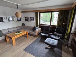 A modern living room with a wooden coffee table, a grey sofa, a black leather armchair, and a small side table. - Floralp 5 # 4-bed apartment, Bad, WC 4-Bettwohnung, Bad, WC by Interhome (Leukerbad)