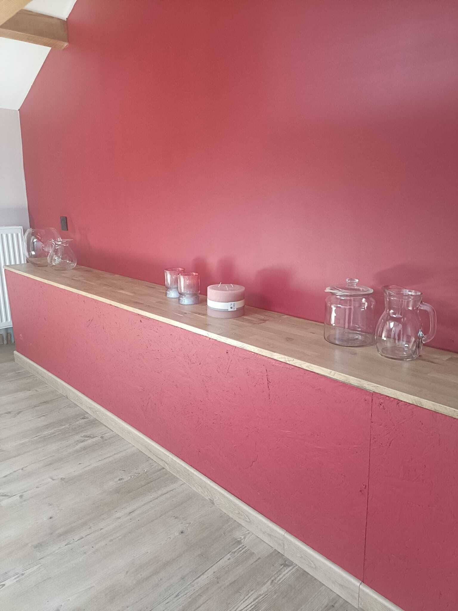 A red wall with a wooden shelf holding glass candle holders and jars.