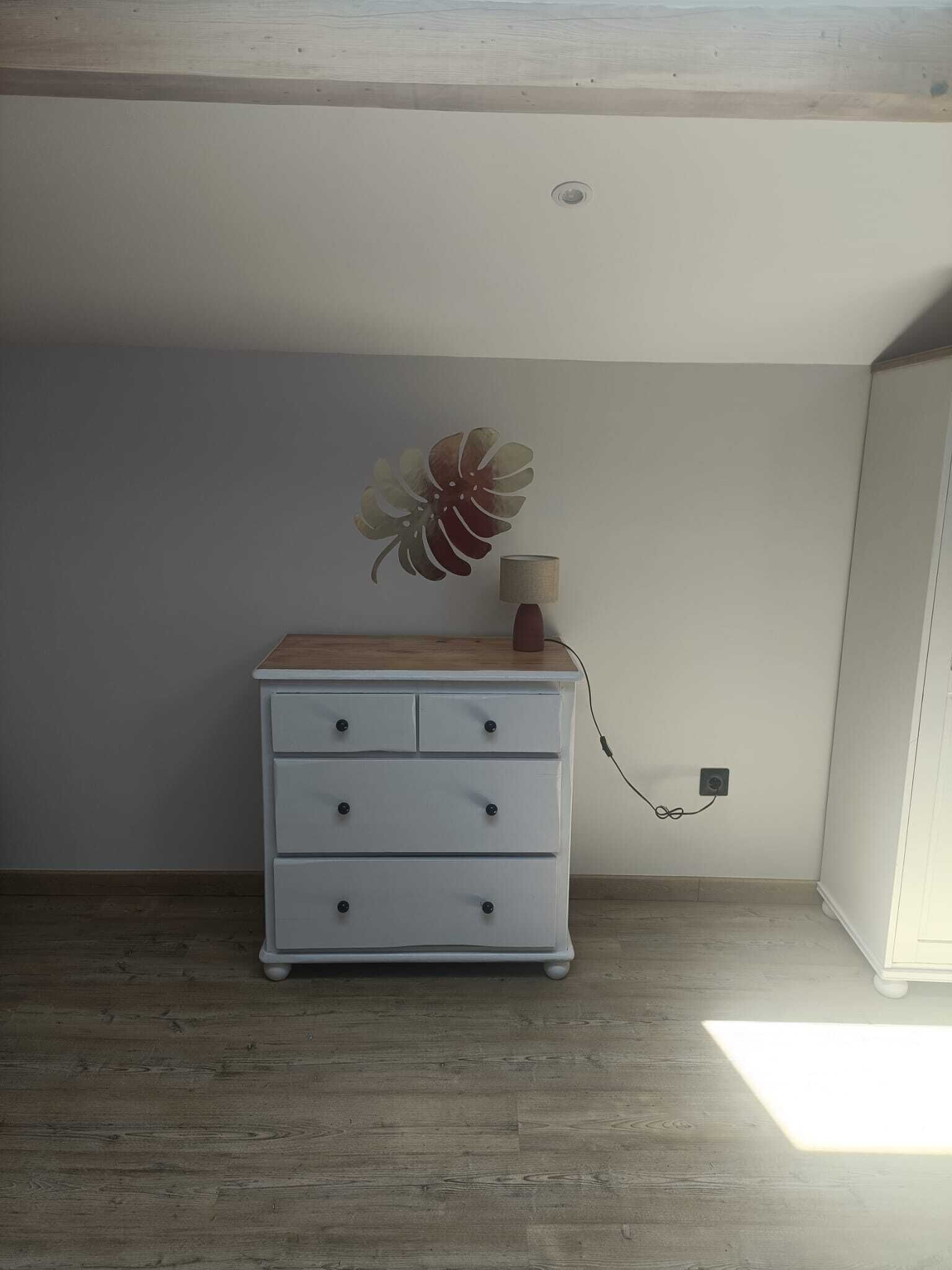 A white dresser with drawers, a wooden top, and a decorative flower piece.