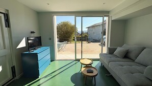 A modern living room with a sofa, a television on a blue cabinet, and a view of a courtyard through large glass doors.