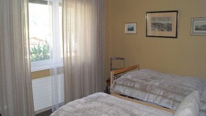 Une chambre avec deux lits, une fenêtre avec des rideaux et deux tableaux encadrés accrochés au mur.