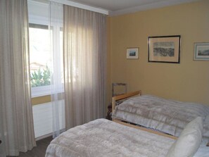 Ein Zimmer mit zwei Betten, einem Vorhangfenster und zwei gerahmten Bildern an der Wand.