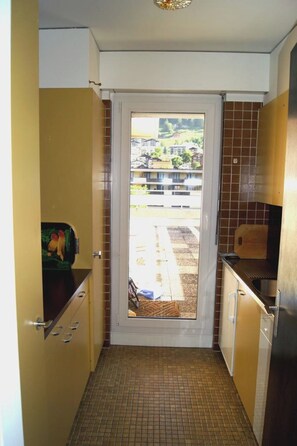 Eine schmale Küche mit einer Tür zu einem Balkon, befliessten Wänden und einem Edelstahl-Kühlschrank.