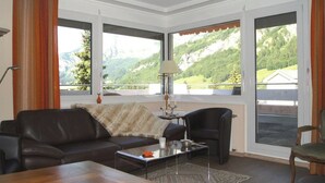 Un salon comprenant un canapé, un fauteuil, une table basse et offrant une vue sur un paysage montagneux grâce à de grandes fenêtres.