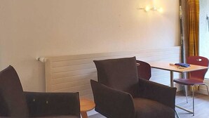 Una habitación con dos sillas de color oscuro, una mesita y una lámpara en la pared.
