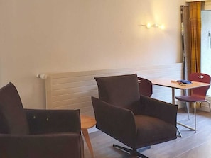 Ein Zimmer mit zwei dunkel gefärbten Stühlen, einem kleinen Tisch und einer Wandleuchte.