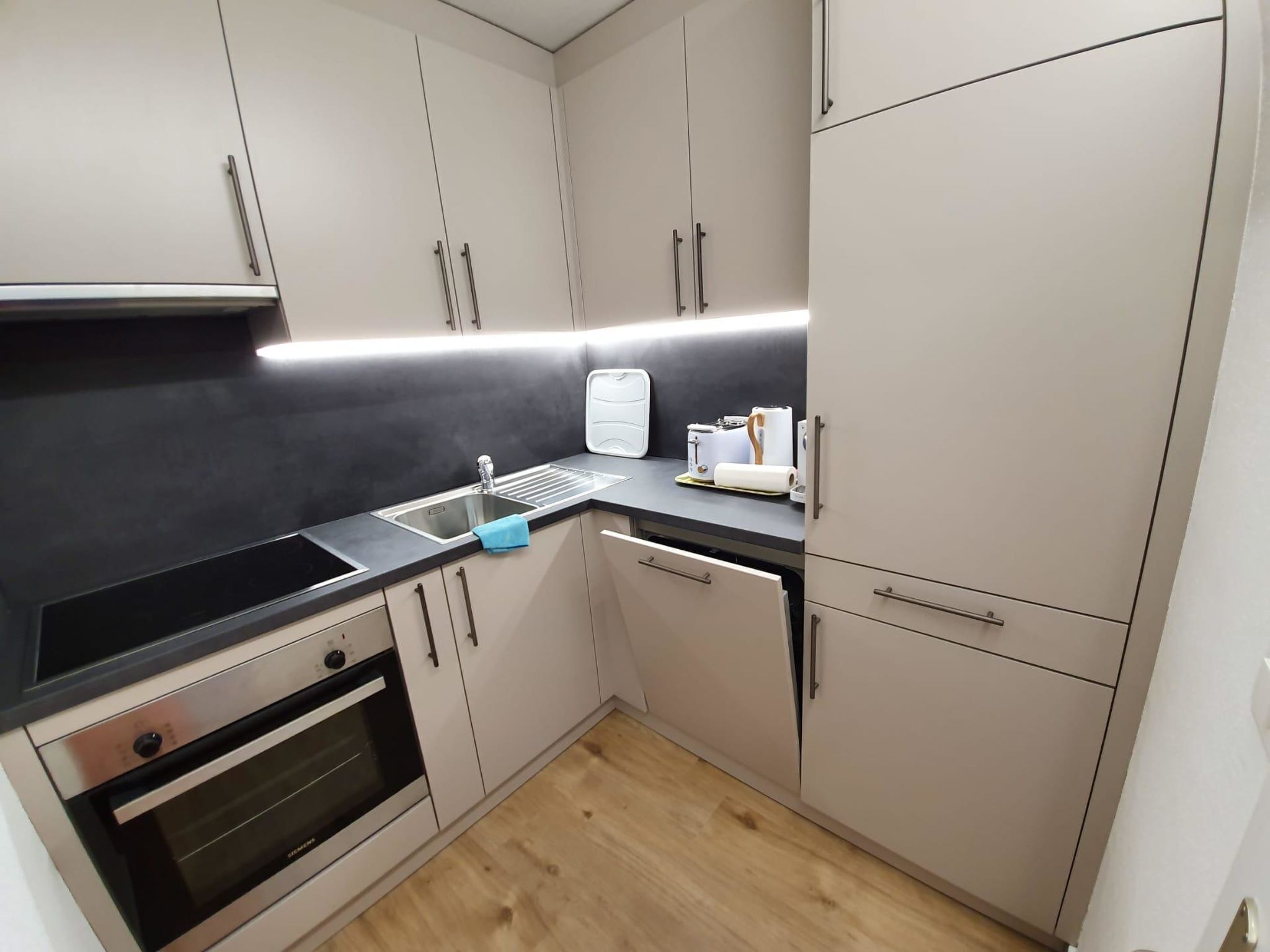 Una cocina moderna con cubierta negra, electrodomésticos de acero inoxidable y armarios de colores claros.