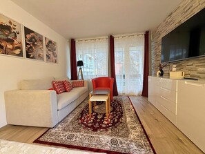 Ein modernes Wohnzimmer mit einer Couch, einem roten Sessel, einem Couchtisch und einem Fernseher.