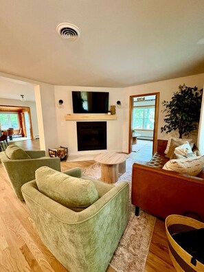 A living room with a fireplace, a television mounted above it, and a large window. - Spacious 5-bedroom house for the whole family (Laconia)