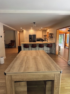 A modern kitchen with white cabinets, a stainless steel refrigerator, and a wooden dining table. - Spacious 5-bedroom house for the whole family (Laconia)
