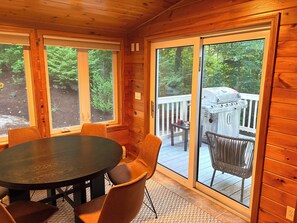A wooden interior with a round table and chairs, a sliding glass door leading to an outdoor deck with a grill. - Spacious 5-bedroom house for the whole family (Laconia)