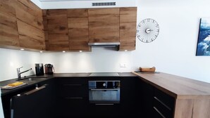 Una cucina compatta con mobili in legno, un forno integrato e una sveglia appesa al muro.