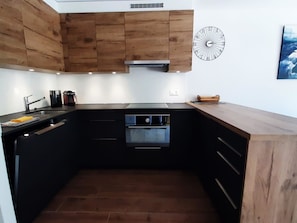 Eine kleine Küche mit Holzschränken, einem eingebauten Backofen und einer Wanduhr.