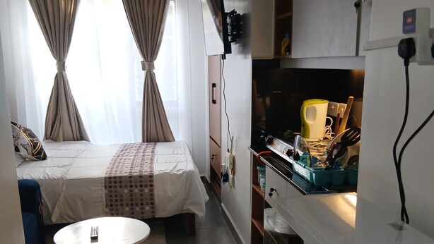 A compact hotel room with a bed, a small round table, a kitchenette, and a TV. - Modern, secure studio with Wi-Fi, Smart TV & kitchenette in Thindigua. (Kiambu)