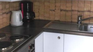 Pieni, käytännöllinen keittiö, jossa on valkoiset kaapit, kaasuliesi, kahvinkeitin ja pesuallas.