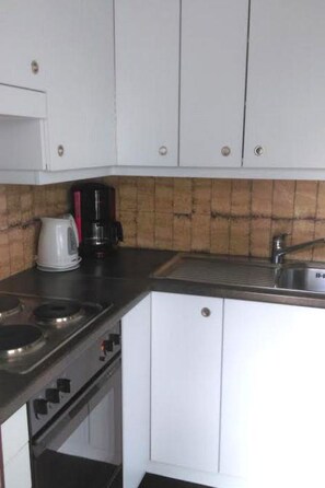 A compact kitchen with white cabinets, a gas stove, a coffee maker, and a sink. - Royal 50 # 4-bed apartment, Dusche, WC 4-Bettwohnung, Dusche, WC by Interhome (Leukerbad)