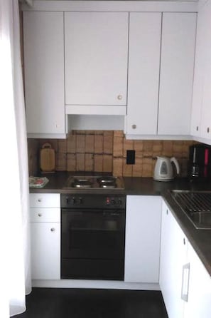 Eine kleine Küche mit weißen Schränken, einem Herd, einem Backofen und einer Kaffeemaschine.