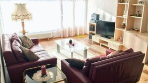 Ein Wohnzimmer mit einer Sofagarnitur, einem Couchtisch, einem Fernseher und einem Bücherregal.