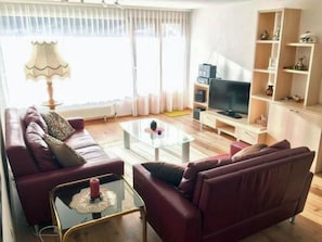 Ein Wohnzimmer mit einer Sofagarnitur, einem Couchtisch, einem Fernseher und einem Bücherregal.