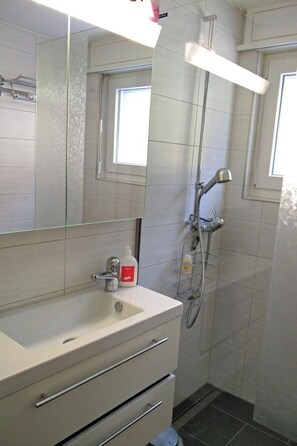 Une salle de bain avec un lavabo blanc, un miroir et une douche.