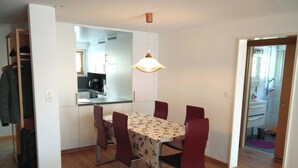 Ein Essbereich mit Tisch und Stühlen, eine Küche im Hintergrund und ein Durchgang zu einem Badezimmer.