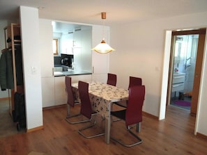Ein Essbereich mit Tisch und Stühlen, eine Küche im Hintergrund und ein Durchgang zu einem Badezimmer.