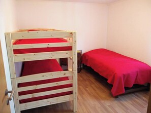 Una habitación con una cama litera y una cama individual, ambas con ropa de cama roja.