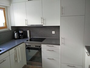 Eine kleine Küche mit weißen Schränken, einem eingebauten Herd und einer Kaffeemaschine.