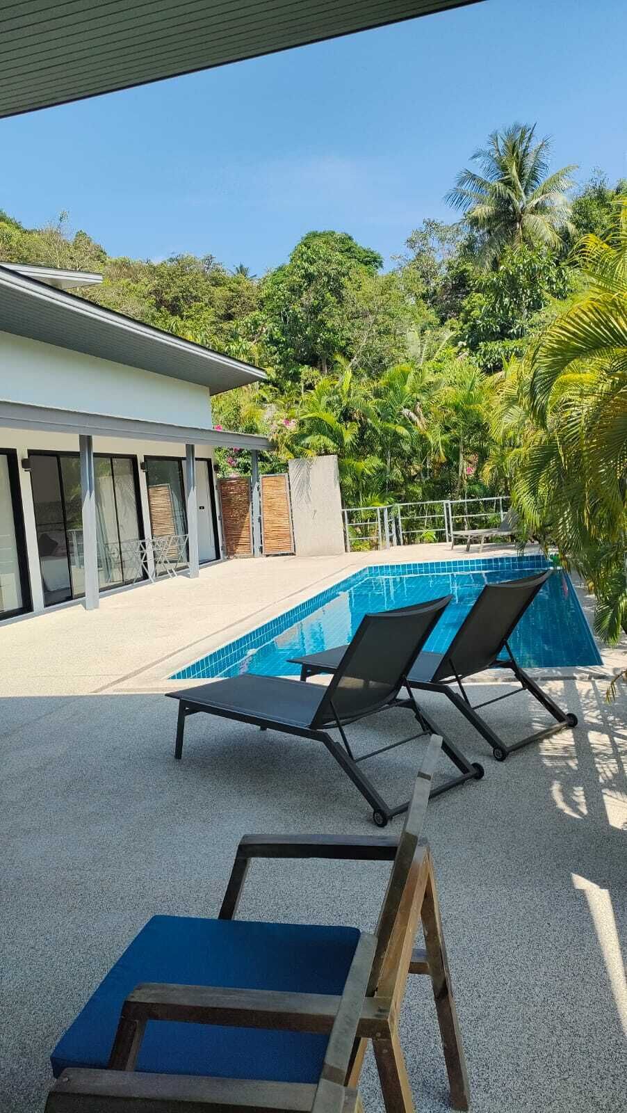 A swimming pool with two lounge chairs, a covered patio, and a building with large windows.