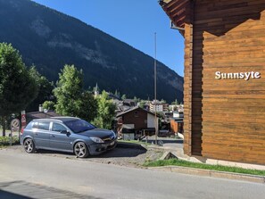 Ein Gebäude mit dem Schriftzug 'Sunnyside' an der Fassade, ein geparktes Auto und eine Bergkulisse.
