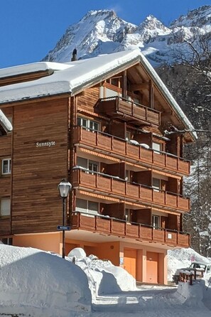 Ein mehrstöckiges Holzhaus mit Balkonen, das 'Sunnyside' genannt wird, umgeben von Schnee und Bergen.