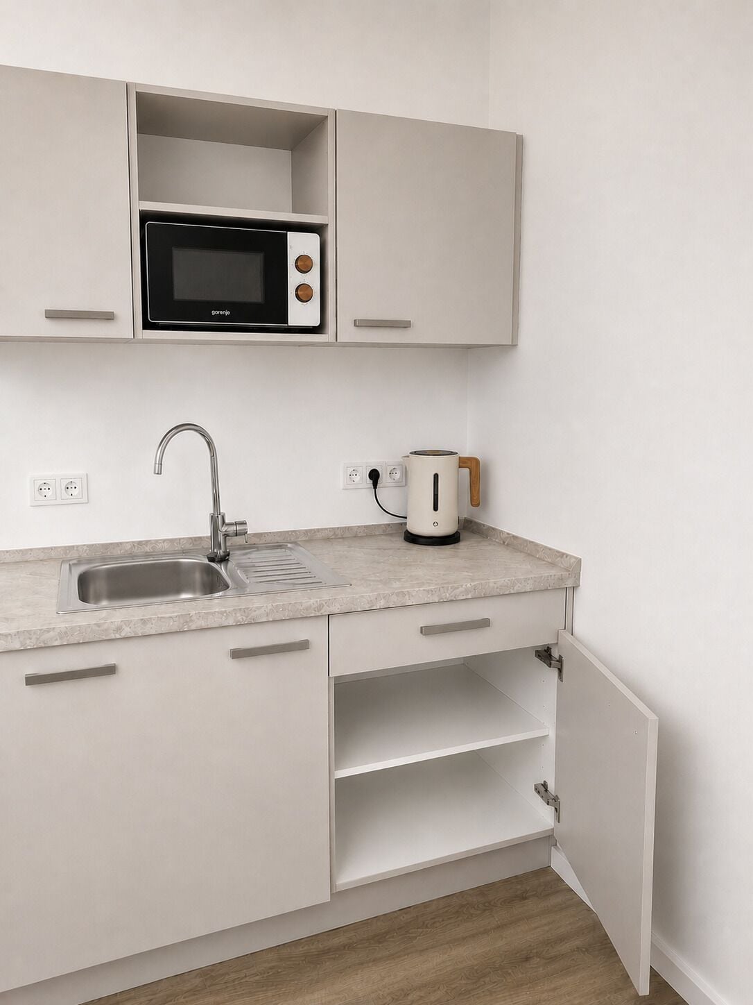 A modern kitchen with a built-in microwave, a sink, and a kettle.
