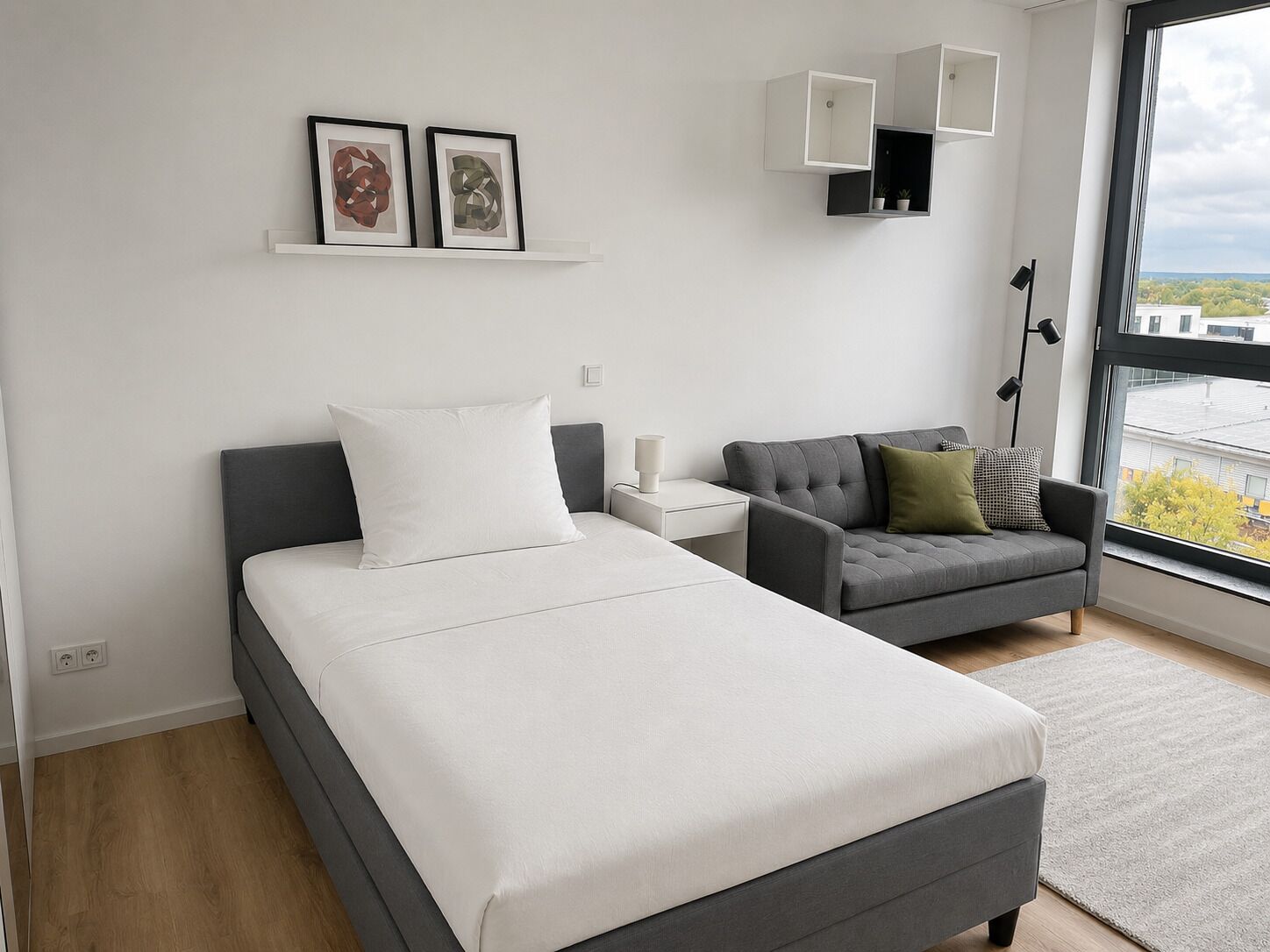 A modern bedroom with a bed, a sofa, a nightstand, and a window with a view.
