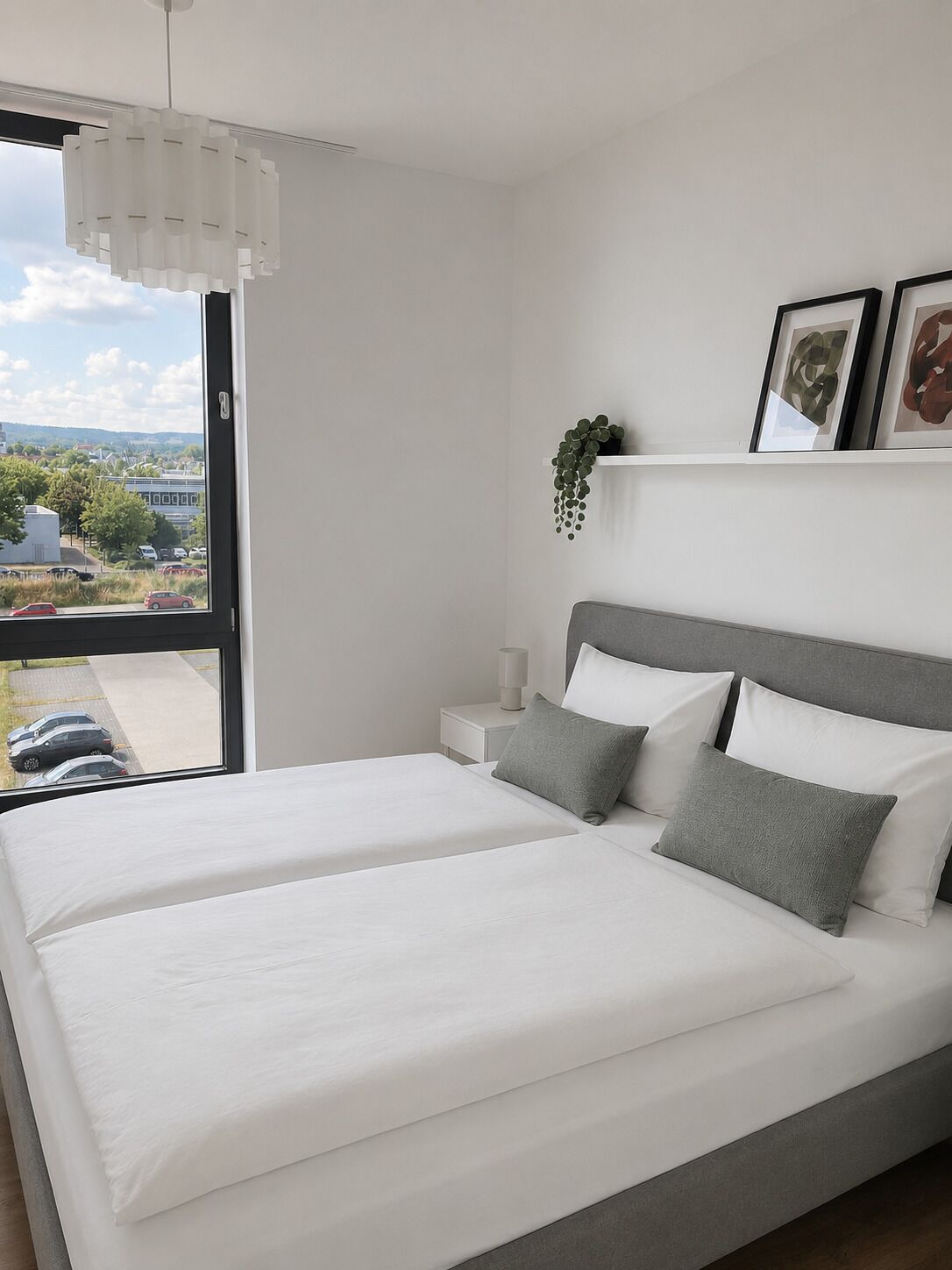 Een moderne slaapkamer met een groot bed, een nachtkastje, een hangplant en lijstwerken aan de muur.