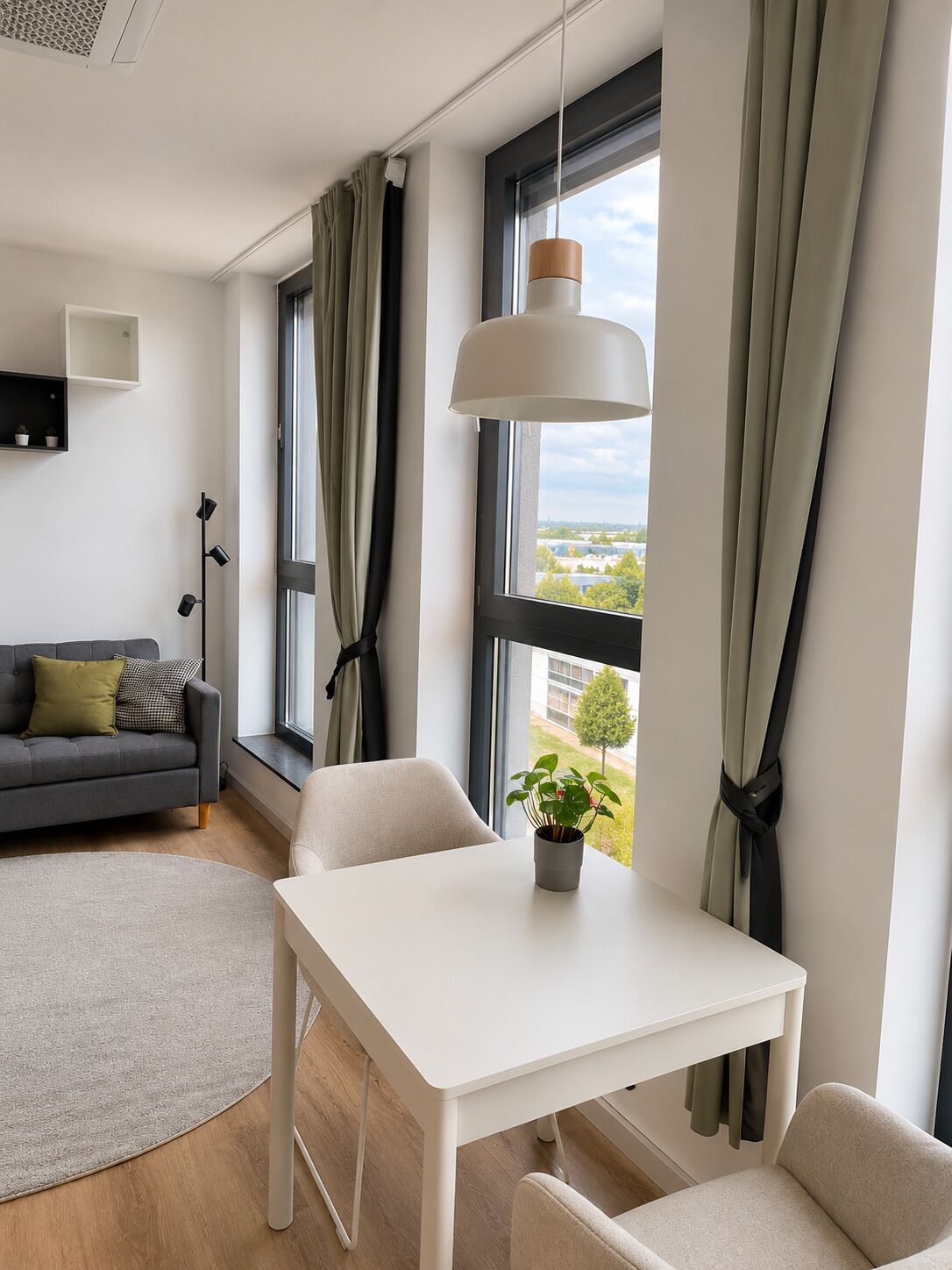 A modern living room with a sofa, a dining table, and a view of the outdoors.