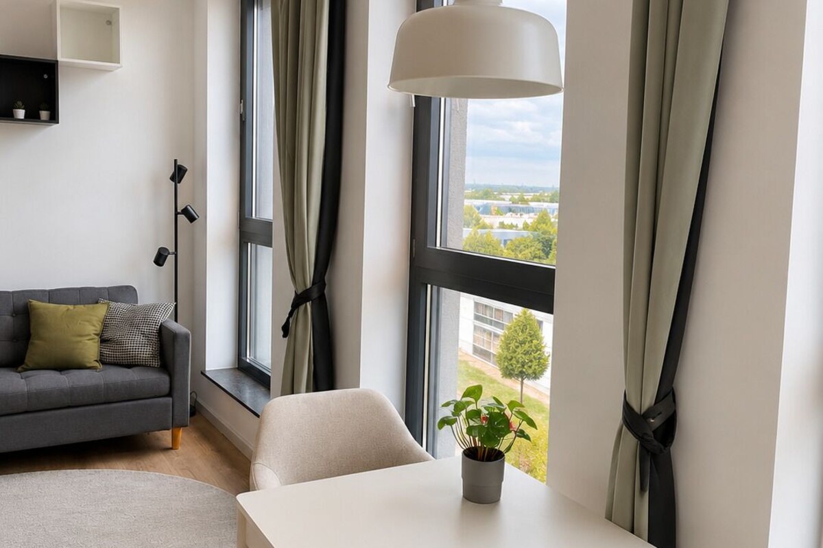 A modern living room with a sofa, a dining table, and a view of the outdoors.