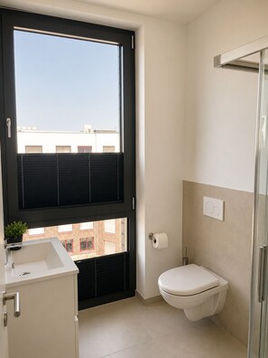 A modern bathroom with a toilet, a sink, and a window with blinds.