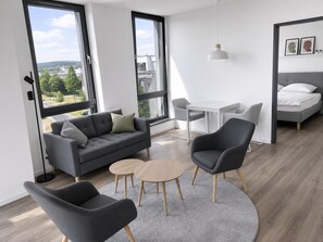 A modern living room with a sofa, two chairs, a small table, and a bed.