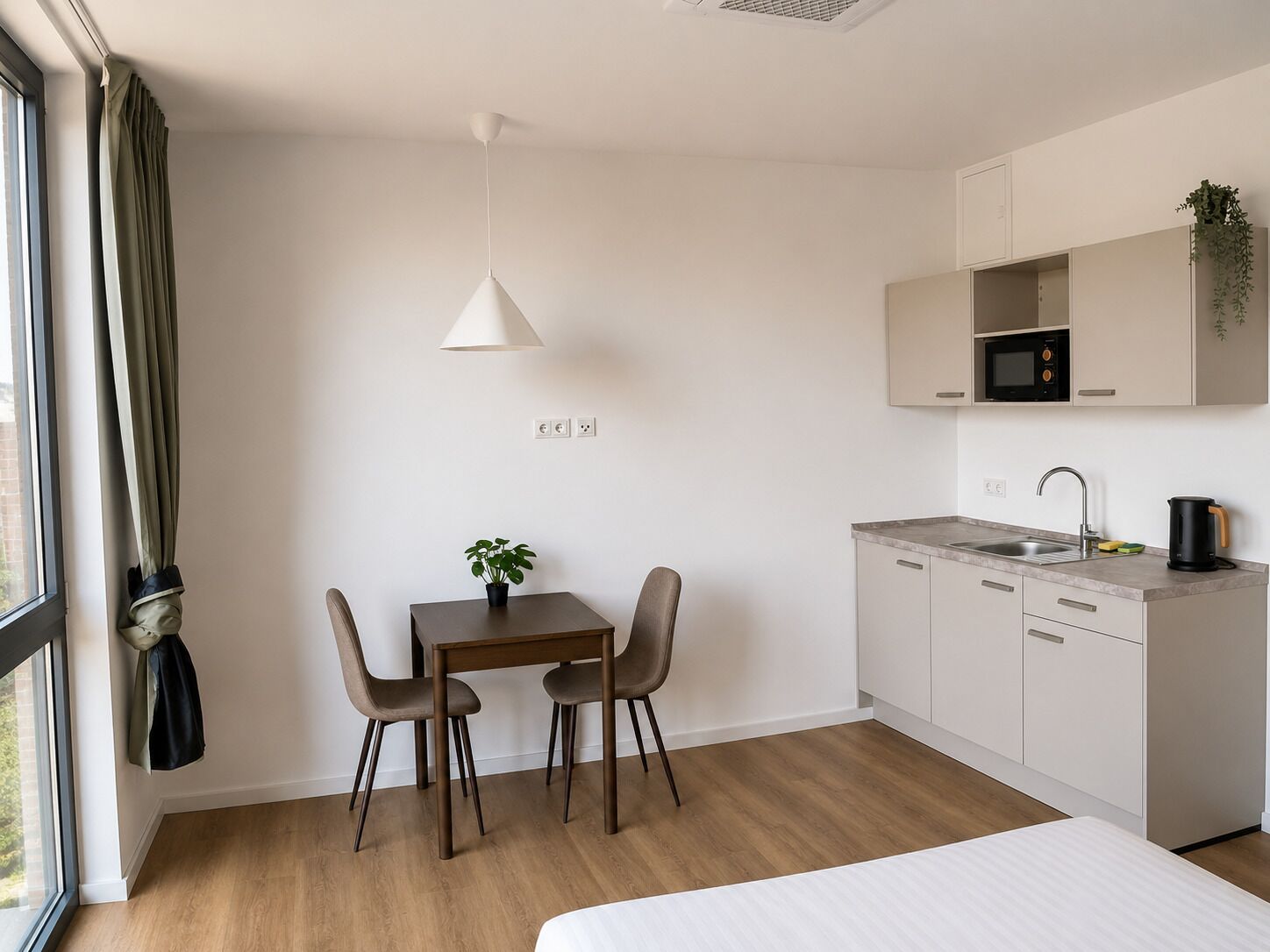 A modern kitchen with a dining area, a single bed, and a window with curtains.
