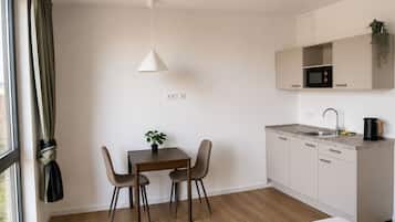 A modern kitchen with a dining area, a single bed, and a window with curtains.