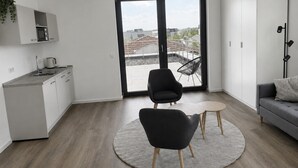 Un apartamento moderno con cocina, un comedor con dos sillas, un sofá y un amplio ventanal corredero que da a un balcón.