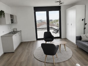 A modern apartment with a kitchen, a dining area with two chairs, a sofa, and a large sliding glass door leading to a balcony. - STAY - Boardinghouse Rheinbach-Bonn (Rheinbach)