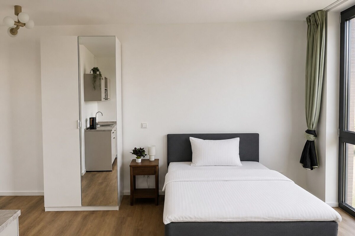 A bedroom with a bed, bedside table, and a view of the outside.