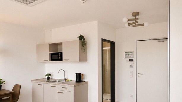 Cocina moderna con microondas, lavabo y cafetera. Hay una mesa de comedor con sillas y una cama en la habitación.