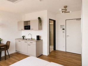 A modern kitchen with a microwave, sink, and coffee maker. There is a dining table with chairs and a bed in the room.