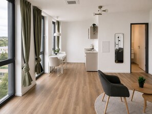 A modern living room with a dining area, a kitchen, and a large window with curtains.