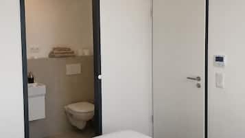 A bedroom with a bed, a door leading to a bathroom, and a wall-mounted light fixture.