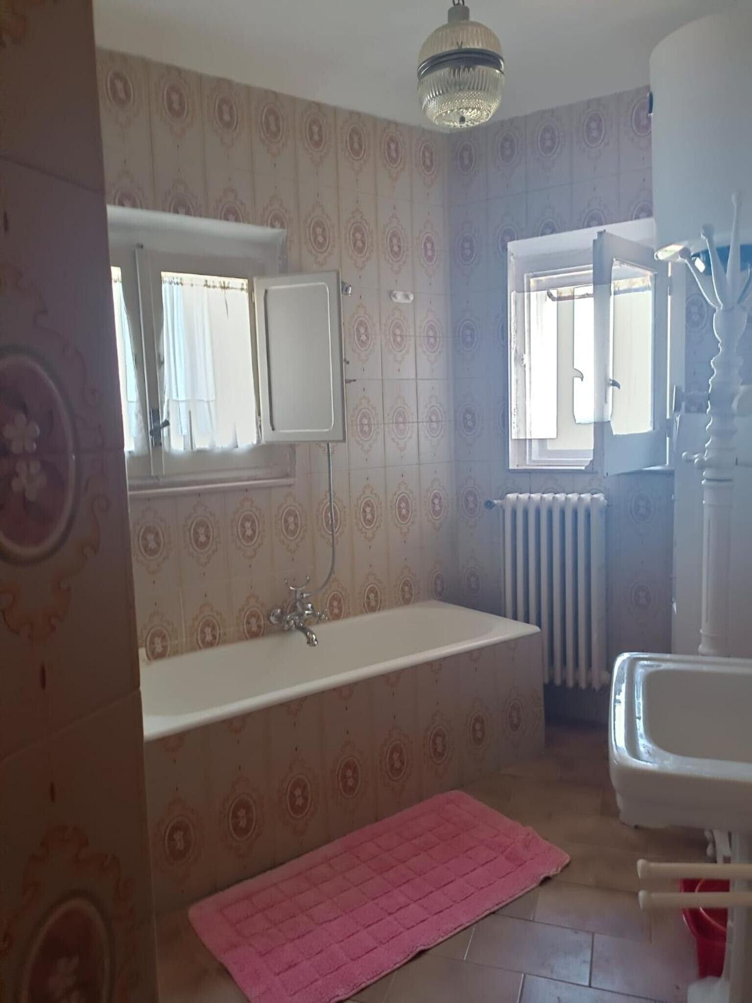 Ein Badezimmer mit Badewanne, Spiegel, Heizkörper und Fenster.
